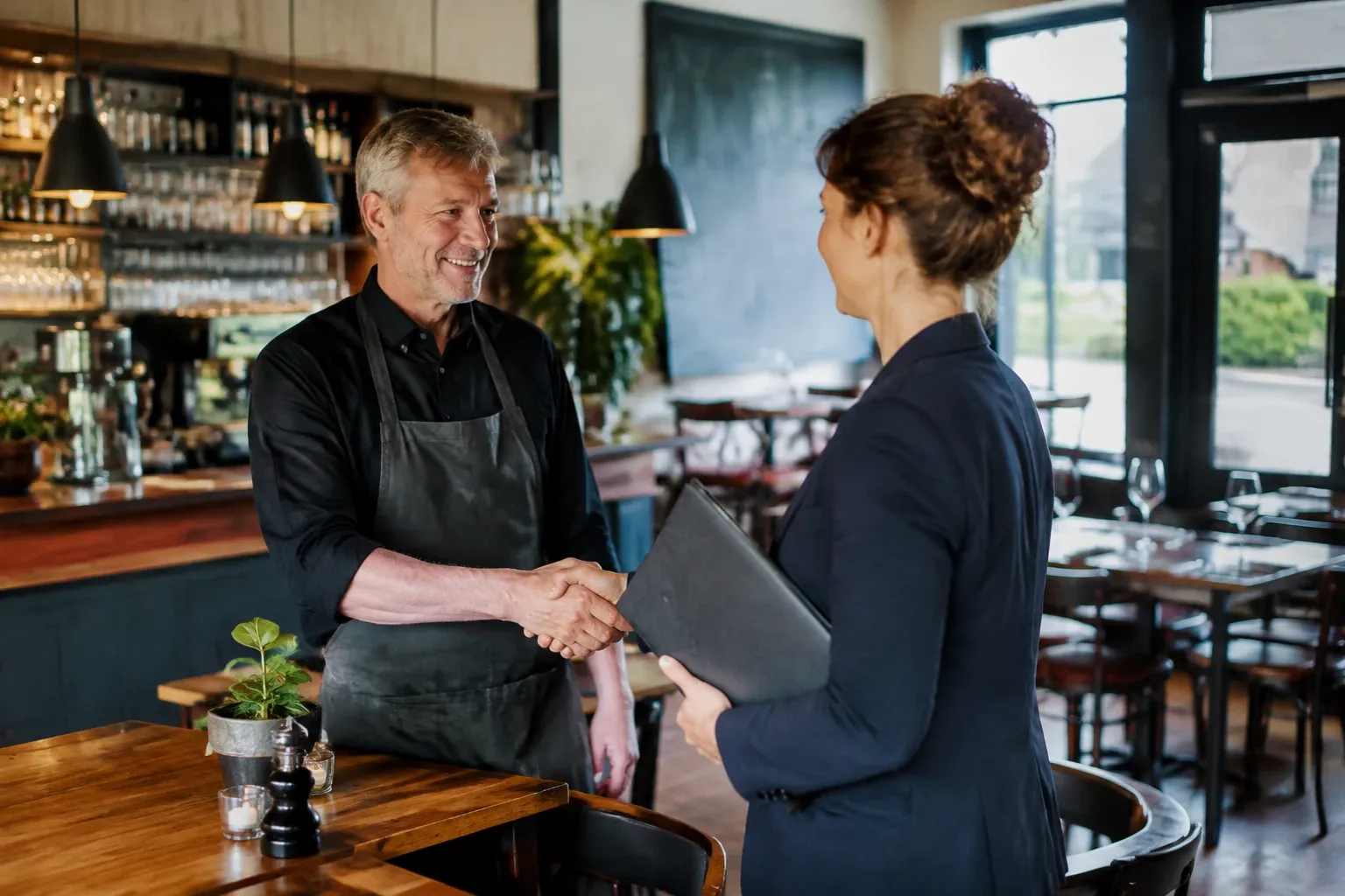 Man met schort en vrouw met map schudden handen in restaurantinterieur